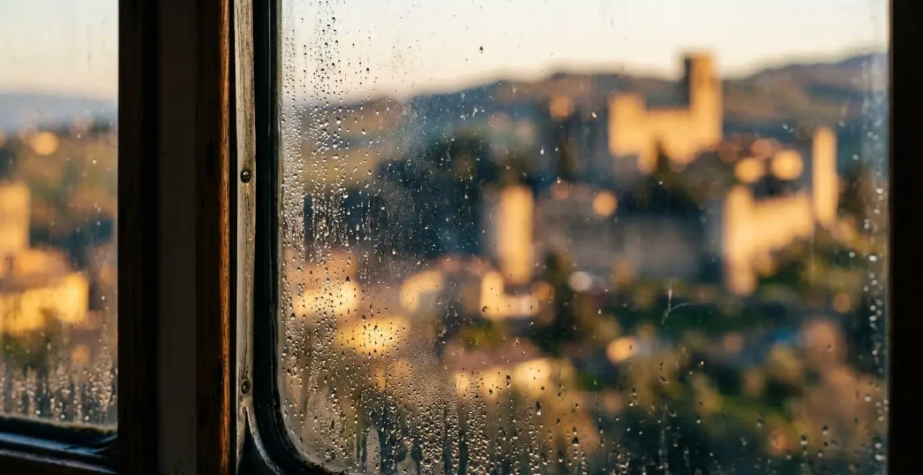 Vue depuis une fenêtre de train sur un paysage de collines avec une cité médiévale au loin