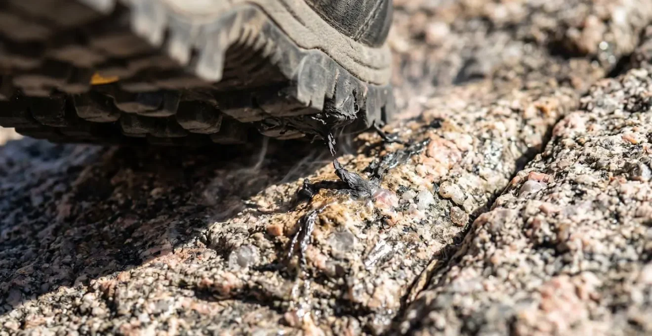 Gros plan macro sur une semelle de chaussure alpine montrant la déformation de la gomme sur une roche granitique surchauffée